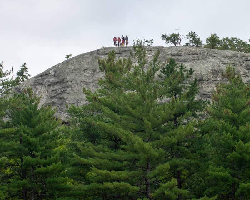 Photo taken looking up at a group of people standing on a giant boulder called Jockey Cap.